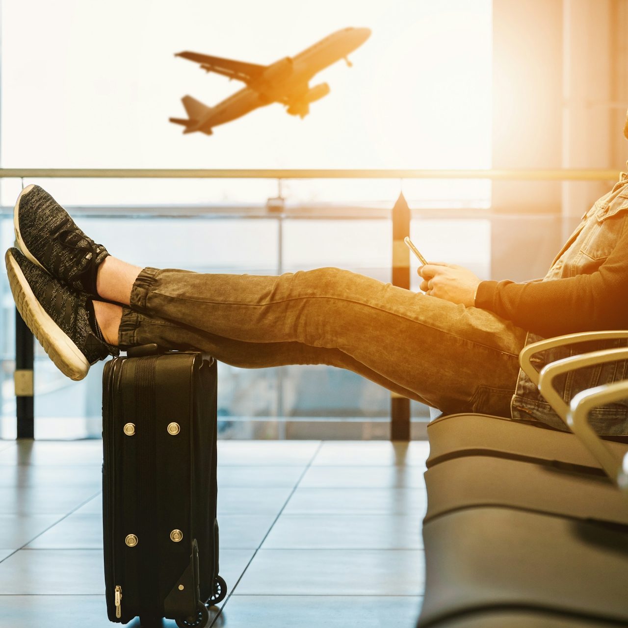 Person resting feet on suitcase in airport, with airplane taking off in background.